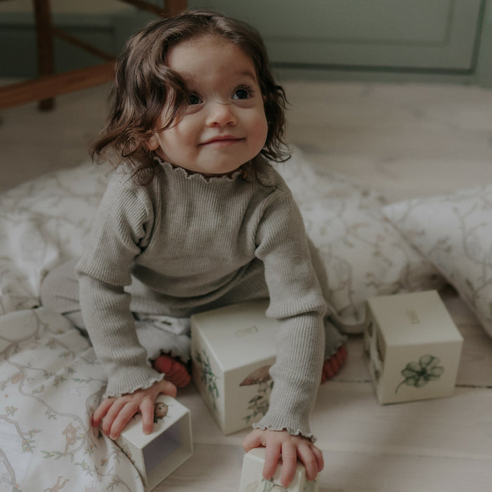 Animal Parade Baby Duvet in Ivory. Child playing on top of duvet with stacking blocks