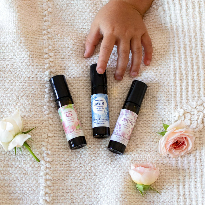Three small perfume bottles with labels on a textured surface surrounded by flowers