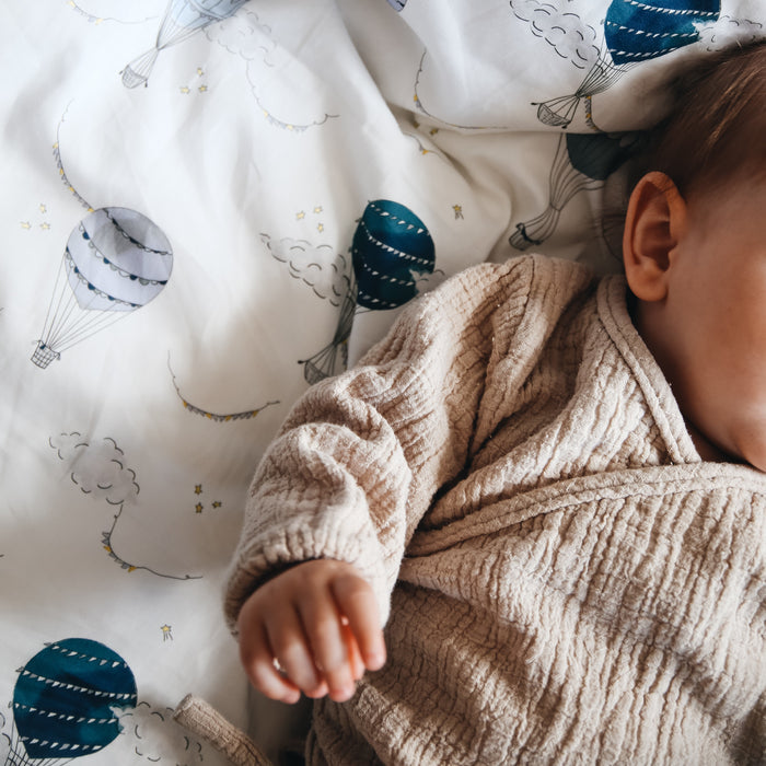 Baby laying on top of gooselings duvet in the print "Touch The Sky" in the color blue