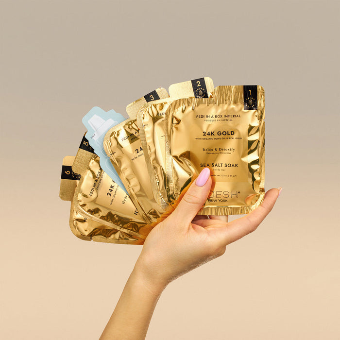 Hand holding gold packets of a skincare product with a beige background