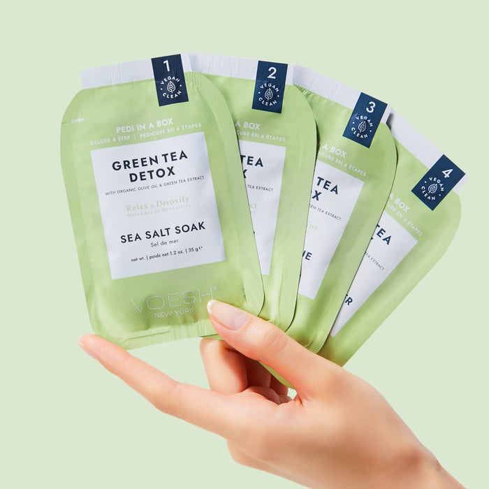 Hand holding green tea detox sea salt soak packages against a light green background
