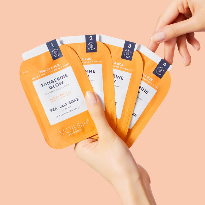 VOESH Tangerine Glow sea salt soaks with a hand holding them against a peach background